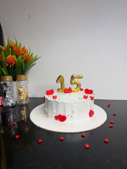A simple and sweet cake for a 15th birthday. The white cake is decorated with red hearts and golden number candles, making it a classic and heartfelt celebration cake.