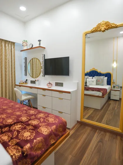 This shot shows the full dresser and TV unit, along with a large, ornate gold-framed floor mirror that enhances the room's sense of space and luxury.