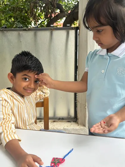 A student ties a rakhi on her friend. During Raksha Bandhan, we teach that "Raksha" means protecting and caring for one another, fostering mutual respect and a safe, supportive community.