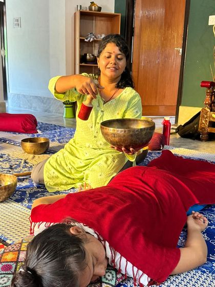 A student practices a one-on-one sound healing session, placing a bowl on the recipient's back to deliver targeted vibrations.