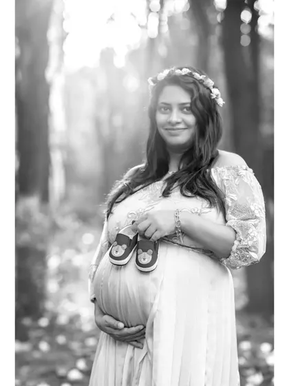 This black and white version of a solo portrait creates a soft, gentle mood. The focus is entirely on the mother's serene expression and the tiny baby shoes she holds.