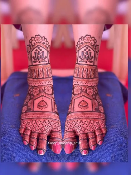 A symmetrical foot design with lotus motifs on the leg and jhumkas on the feet. The dark stain makes the intricate patterns stand out beautifully.