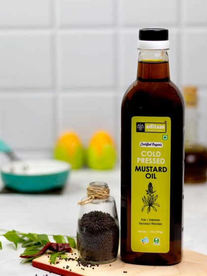 This shot of cold-pressed mustard oil is styled with mustard seeds and curry leaves in a clean kitchen setting. The bright lighting and simple props highlight the product's everyday utility.