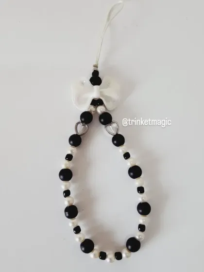 A simple and elegant black and white phone strap, featuring pearl-like beads and a delicate white bow.