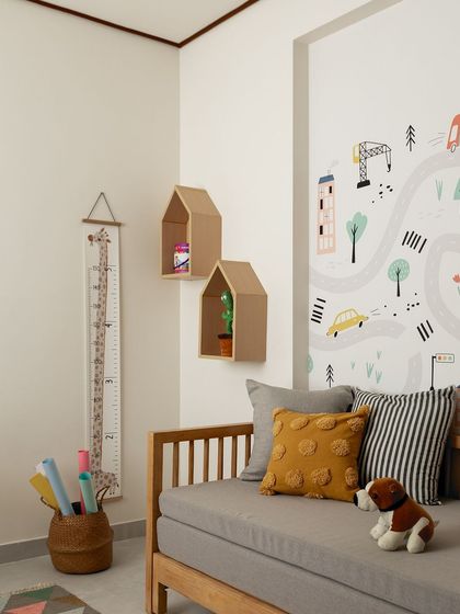 This room is designed for a young child, with a simple daybed, house-shaped wall shelves, and a fun road-map wallpaper. The yellow and grey cushions add a pop of color to the otherwise neutral and calming space.
