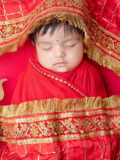 A divine little Maata Rani, sleeping peacefully under a traditional red and gold chunari.