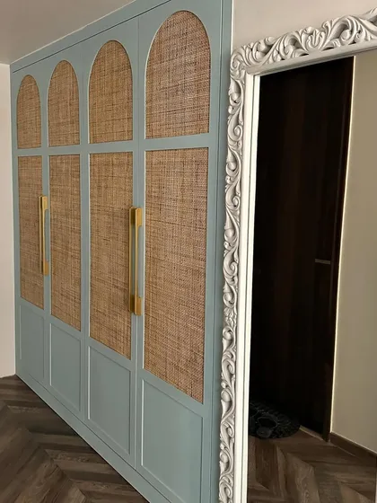 A custom wardrobe with arched cane-paneled doors in a soft blue, paired with a beautifully carved mirror frame for a touch of vintage charm.