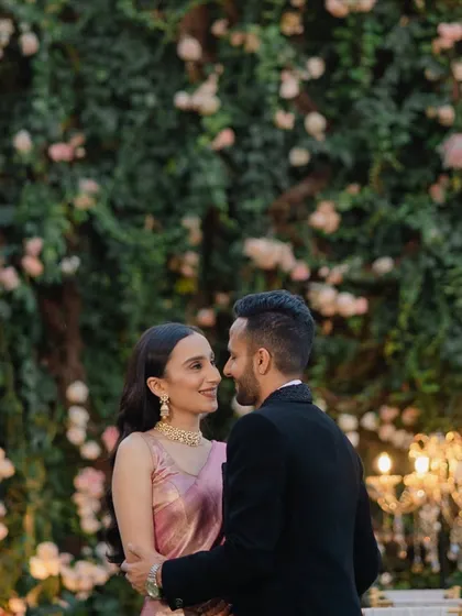 An intimate portrait of the couple against a wall of flowers, with soft lighting creating a romantic and dreamy atmosphere.