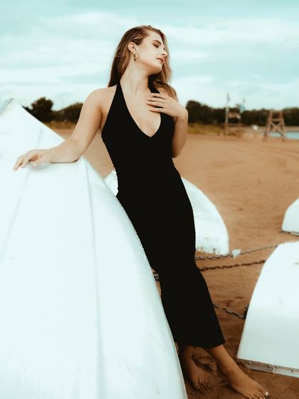 A graceful and elegant pose, with the model's body creating a beautiful line against the simple white boat on the beach.