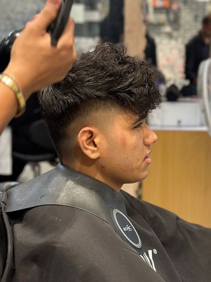 A side view of the men's curly haircut in progress, showing the stylist using a blow dryer to set the style.