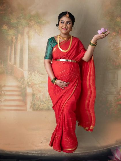 Posing with a lotus flower, this mom-to-be embodies grace and serenity. The soft, painted background enhances the artistic and timeless quality of this saree portrait.