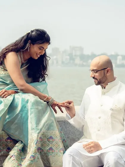 A beautiful outdoor engagement moment with the Mumbai skyline in the background, as the ring is placed on her finger.