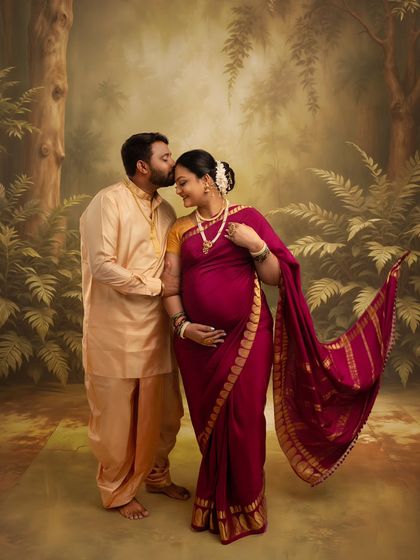 A tender forehead kiss in a forest setting. This Ravi Varma-style portrait captures the protective and loving embrace of the father-to-be, wrapped in traditional attire.