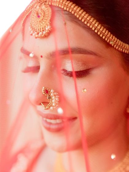A close-up of the bride's face through her veil, focusing on the delicate eye makeup and traditional nath. This is a classic and timeless bridal portrait.