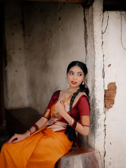 A portrait of a model seated against a rustic wall, looking thoughtfully to the side. The composition and lighting create a classic, painting-like feel.