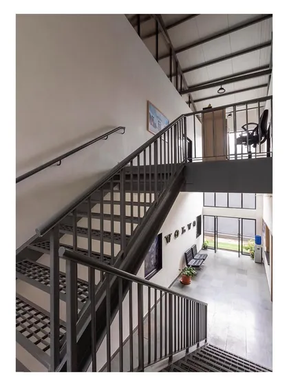 The central staircase connects the ground floor reception with the first-floor offices. The design is open and industrial, using steel and a simple, functional aesthetic to optimize space and light.