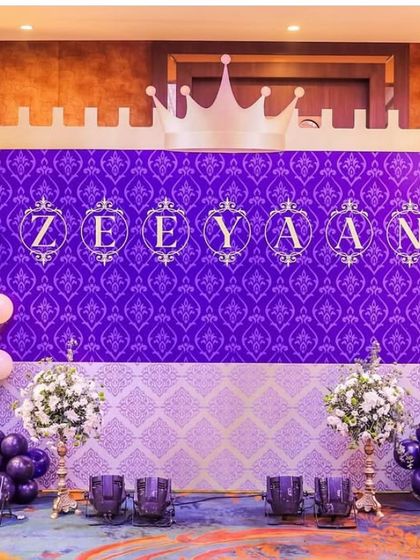 The main stage for Prince Zeeyan's first birthday. A deep purple damask backdrop with his name in ornate lettering is topped with a castle silhouette and framed by beautiful balloon garlands.