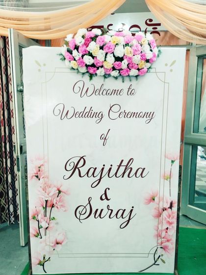 A close-up of a custom wedding welcome sign, featuring elegant calligraphy and a floral motif. Topped with a fresh arrangement of pink and white roses, this sign adds a personal and sophisticated touch to the event entrance.