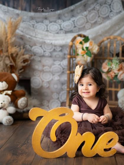 A sweet and simple first birthday portrait. The wooden 'One' sign and rustic backdrop with teddy bears create a warm and timeless feel for this milestone photo.