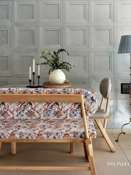 A cozy dining bench with a floral quilted cover brings a touch of farmhouse charm to this space. The paneled grey wall and wicker tray centerpiece add layers of texture.