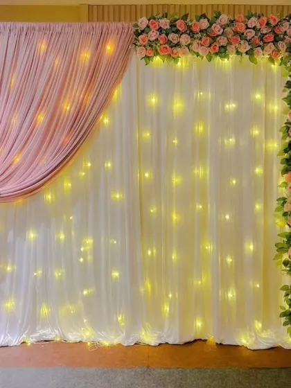 A simple yet elegant backdrop for any function. This design uses a combination of white and dusty pink drapes with a floral border and fairy lights for a soft, romantic glow.