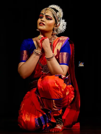 An expressive, kneeling pose from a classical dancer. The dark background helps to highlight the emotion and detail of the performance.