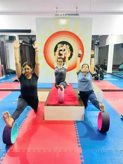 A group of students using yoga wheels to assist in a standing split variation. This shows the versatility of props in a group class setting for all levels.