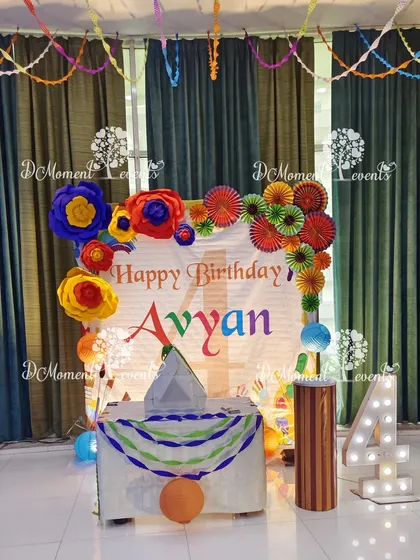 A creative and colorful Art & Craft themed birthday for a 4-year-old. Instead of balloons, the backdrop is decorated with handmade paper flowers and pinwheels, with a light-up number "4" and a craft-themed cake table.