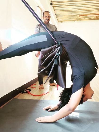 A student practicing a wall-supported backbend with a sling. This builds strength in the legs and arms while opening the entire front body.