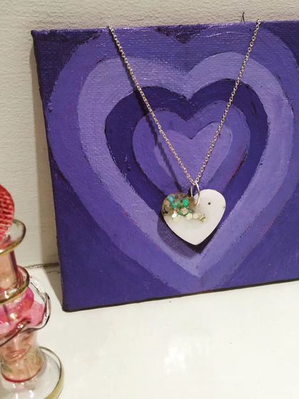 This heart-shaped pendant has a modern design, with a solid white base and a corner filled with crushed green stones. It's a unique take on the classic heart necklace.