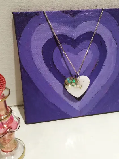 A heart shaped necklace pendant with a mix of white and green floral pieces.