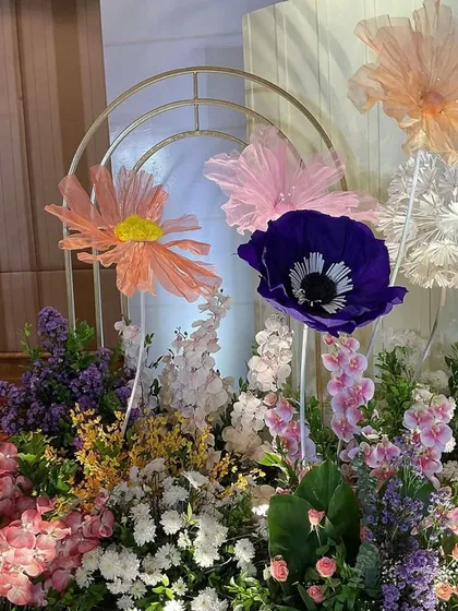 A close-up of the floral arrangement, showing the mix of fresh flowers and large, handcrafted paper flowers in vibrant colors. Golden arches add a touch of modern elegance.