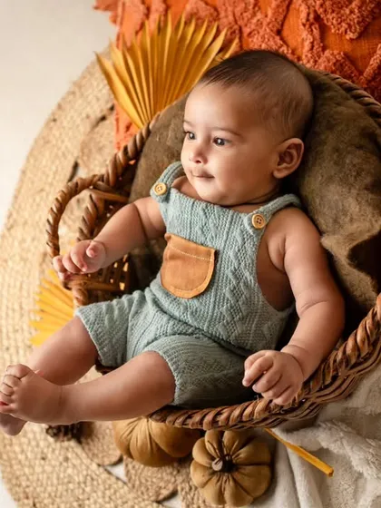 A calm and curious 4-month-old baby relaxing in a basket. The autumn-themed props add a warm and cozy feel to this infant portrait.