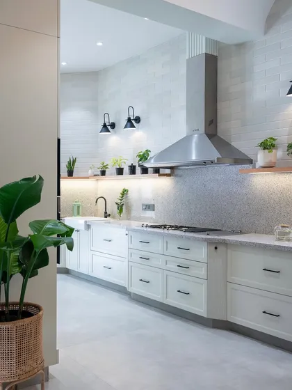 A white kitchen doesn't have to be stark. Here, we layered textures like the brick-patterned wall tiles and terrazzo-style countertops, and added warmth with open wooden shelving and plants to create a space that feels bright, airy, and full of life.
