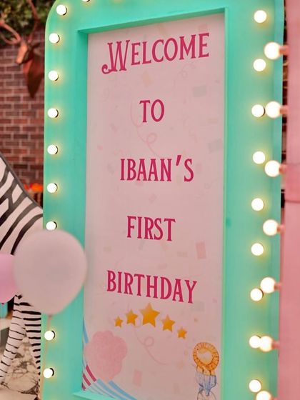 A welcoming marquee sign for Ibaan's first birthday, framed with warm lights. A friendly zebra prop and balloons complete the festive entrance.