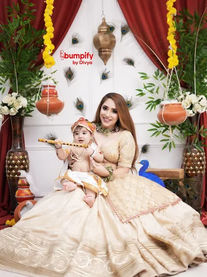 A mother's love for her little Krishna. This elegant Janmashtami portrait features a mom and her baby in a beautiful white and gold themed setup with peacock feathers.