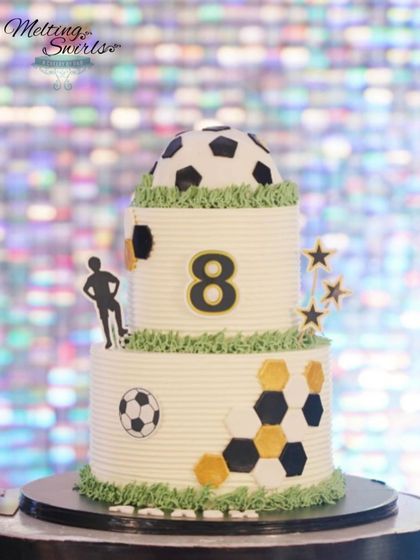 A custom two-tier football themed cake for an 8th birthday. This design features a 3D soccer ball on top and hexagonal patterns, all on a whipped cream base.