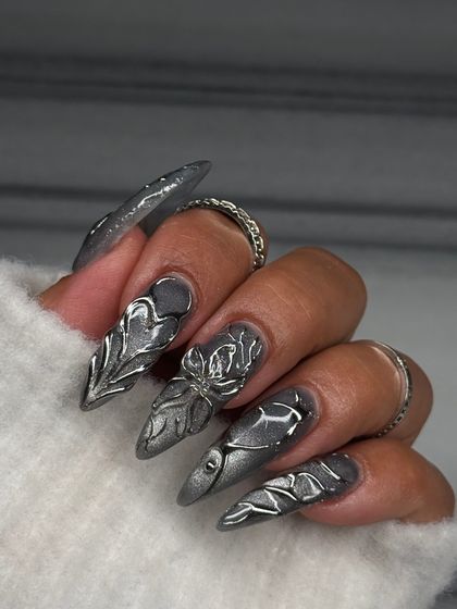 A closer look at the detail in this sculpted silver set. Each nail features a unique, hand-formed metallic design over a shimmering gunmetal base, creating a futuristic and edgy stiletto look.