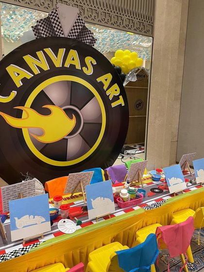 The canvas art station at our Hot Wheels party, complete with a giant tire backdrop, pre-drawn canvases, and colorful aprons for the little racers.