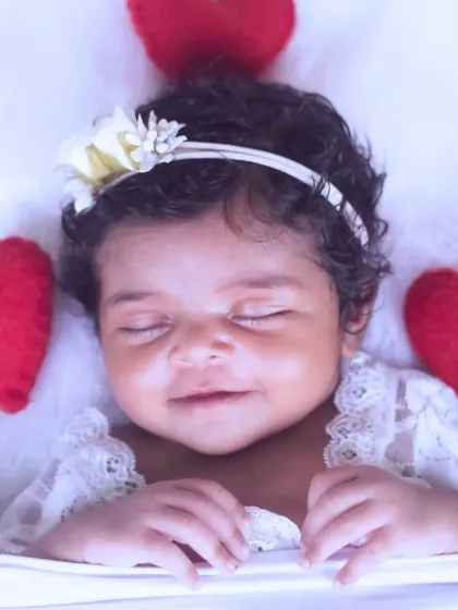 A beautiful sleeping newborn surrounded by soft red hearts, with a lovely floral headband, creating a picture of pure love.