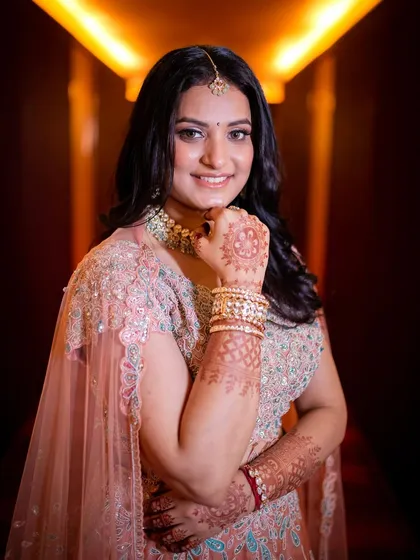 A beautiful portrait of the bride-to-be in her engagement lehenga, smiling brightly in a warmly lit corridor.
