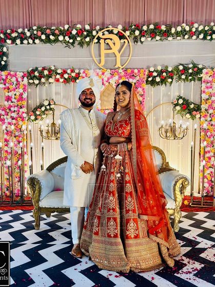 The happy couple posing on the wedding stage I designed. The backdrop features panels of dense flowers, a custom monogram, and elegant floor lamps.