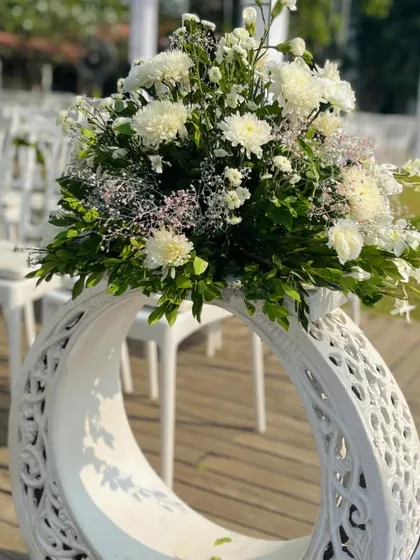 An aisle marker featuring a lush arrangement of white chrysanthemums and baby's breath atop a beautifully carved reusable stand. This detail adds a touch of sophistication and elegance to the wedding ceremony path.
