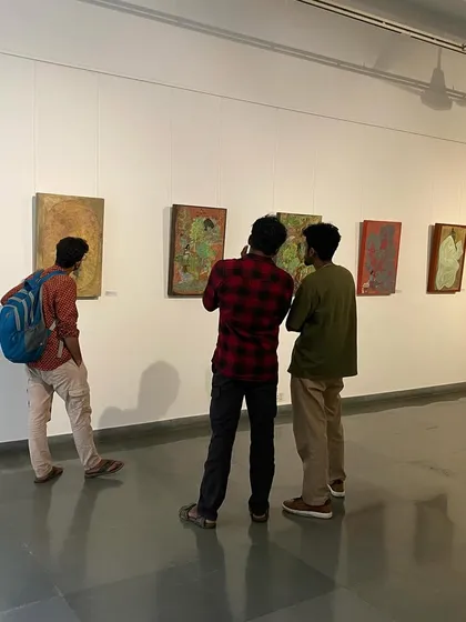Visitors at the 'ME, AMMA, WE' exhibition, looking at the vibrant paintings by Devu Nenmara.