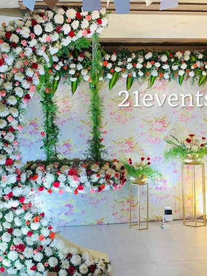 A modern naming ceremony setup featuring a unique cradle shaped like a crescent moon, made entirely of flowers. The floral print backdrop adds a touch of elegance and charm.