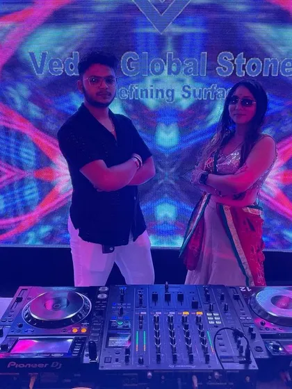 Standing by my DJ console with a colleague at a Garba night for Vedas Global Stones, surrounded by a psychedelic visual backdrop.