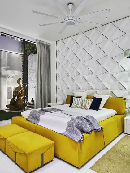 A pop of color can transform a space. This vibrant bedroom was designed with a tale of contrast, where a bright yellow bed and sofa stand against a textured white wall, creating an exuberant and joyful atmosphere.