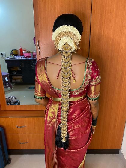 A full view of a traditional bridal braid against a wooden door, highlighting the intricate details. The hairstyle features a jasmine gajra and a complete set of coin-style temple jewellery.