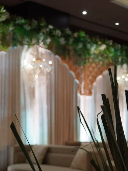 A creative shot of the lounge area, with the focus on the elegant backdrop of drapes, jali work, and hanging greenery.