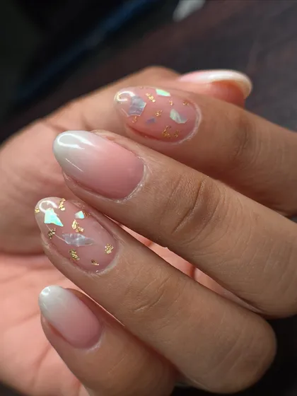 An inbuilt art design featuring a soft ombré base with delicate shell pieces and gold foil encapsulated within the nail.